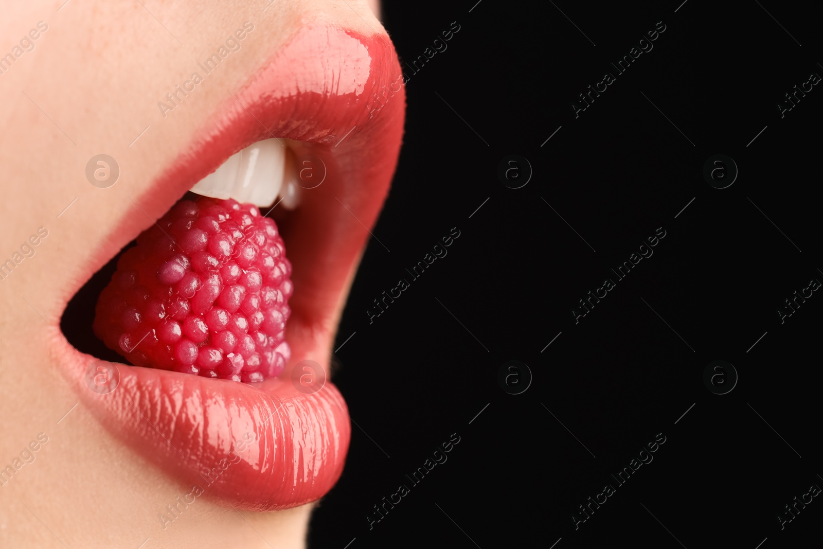 Photo of Woman with beautiful lips makeup and raspberry candy on black background, closeup. Space for text