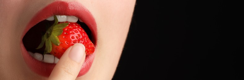 Photo of Woman with beautiful lips makeup and strawberry on black background, closeup. Space for text