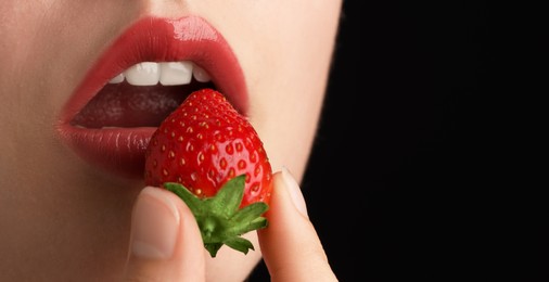 Photo of Woman with beautiful lips makeup and strawberry on black background, closeup. Space for text