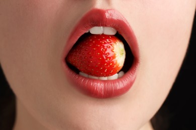 Photo of Woman with beautiful lips makeup and strawberry on black background, closeup