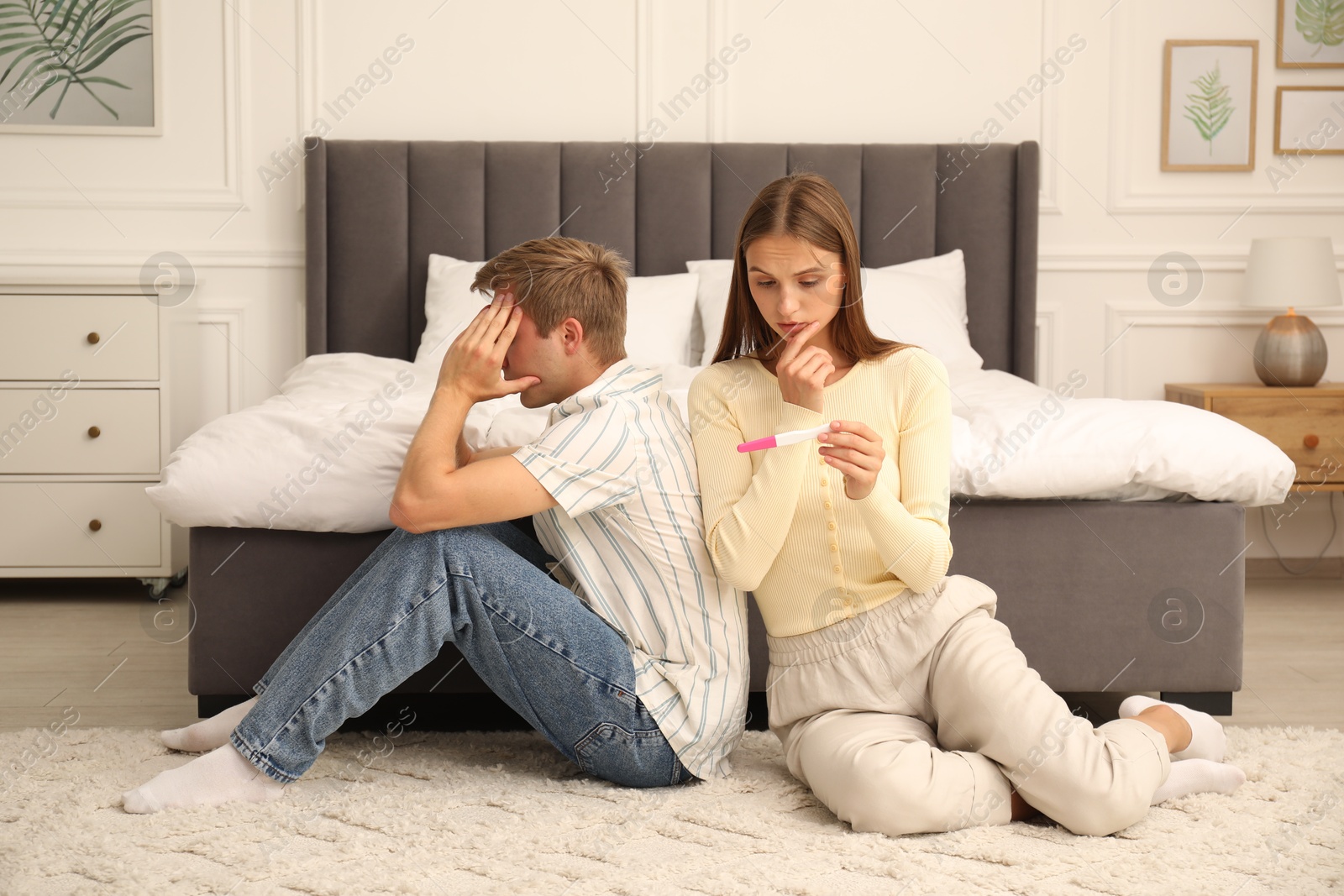 Worried couple with pregnancy test on floor in bedroom Photo of Worried couple with pregnancy test on floor in bedroom