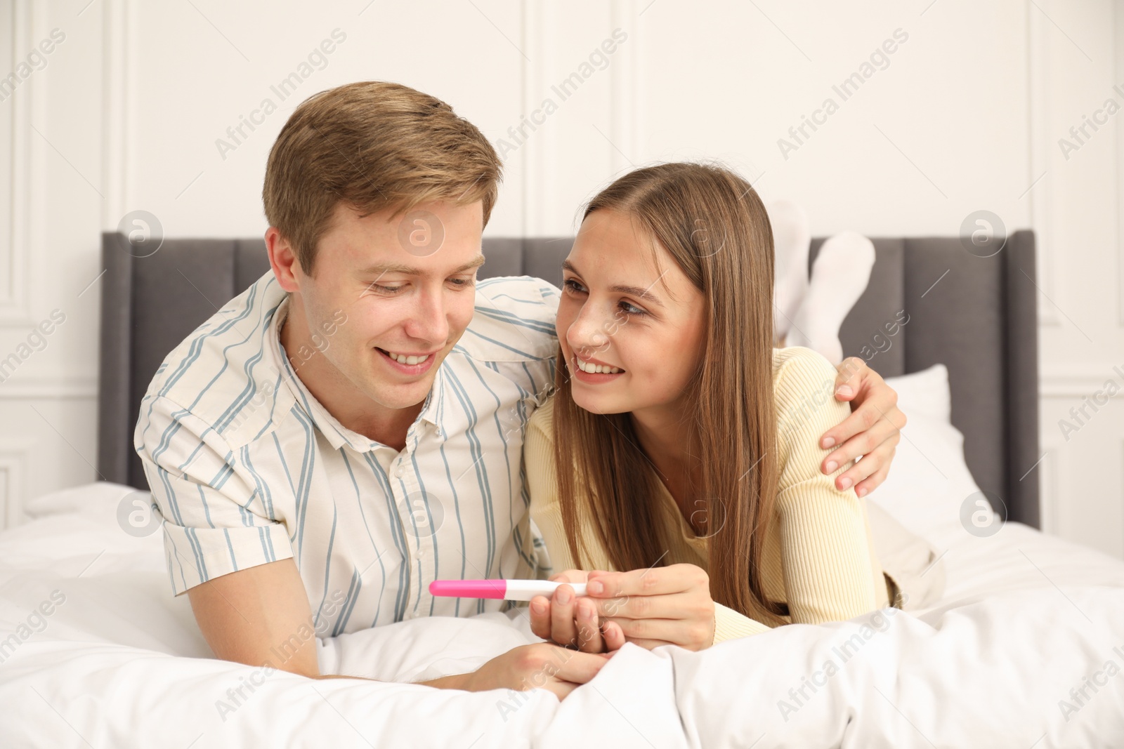 Happy couple with pregnancy test on bed at home Photo of Happy couple with pregnancy test on bed at home