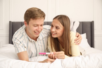 Photo of Happy couple with pregnancy test on bed at home