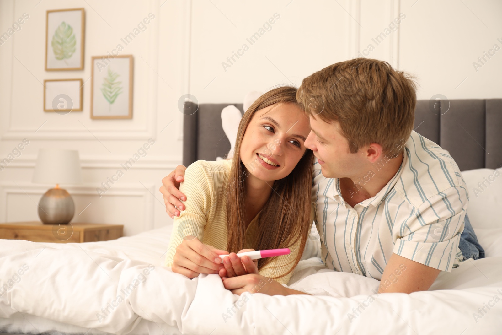 Photo of Happy couple with pregnancy test on bed at home