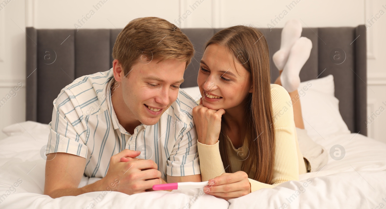 Happy couple with pregnancy test on bed at home Photo of Happy couple with pregnancy test on bed at home
