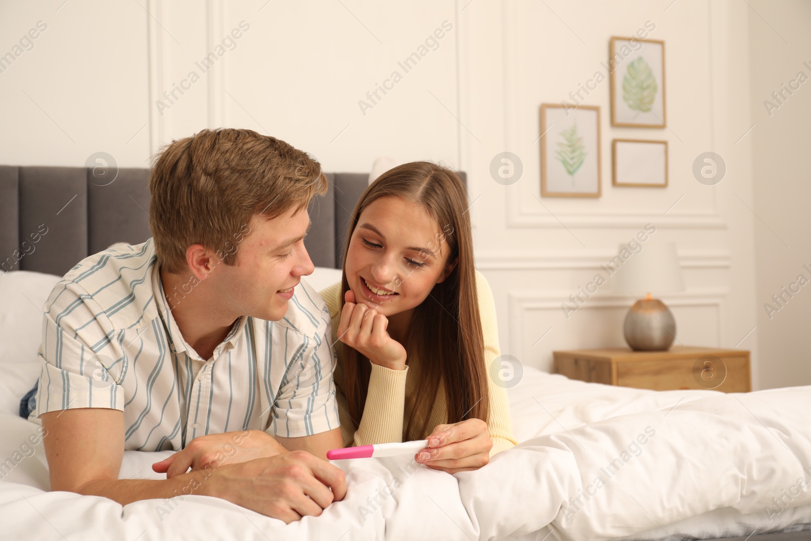 Happy couple with pregnancy test on bed at home Photo of Happy couple with pregnancy test on bed at home