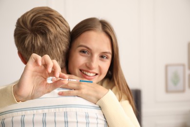 Photo of Happy couple with positive pregnancy test at home, space for text