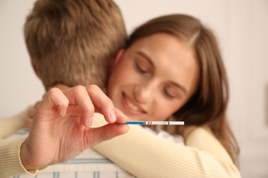 Photo of Happy couple with pregnancy test at home, selective focus