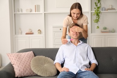 Photo of Happy young woman surprising her husband with positive pregnancy test at home
