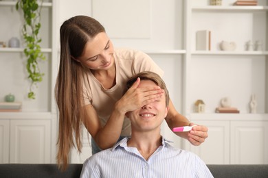 Photo of Happy young woman surprising her husband with positive pregnancy test at home