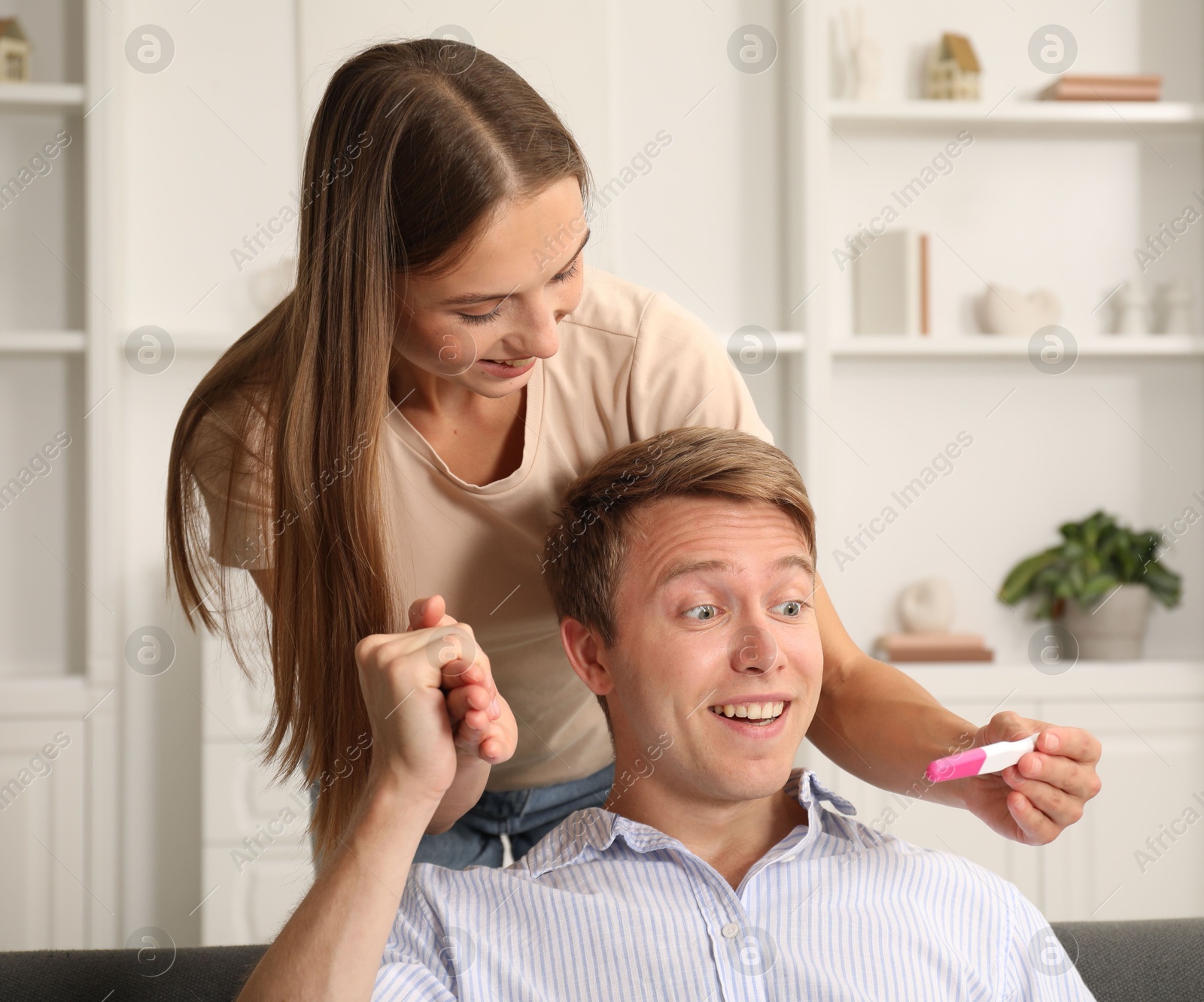 Happy young woman showing her pregnancy test to husband at home Photo of Happy young woman showing her pregnancy test to husband at home