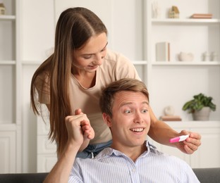 Photo of Happy young woman showing her pregnancy test to husband at home