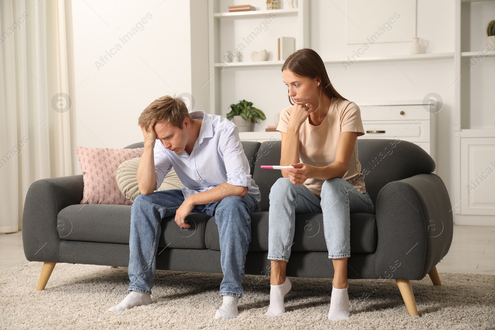 Worried couple with pregnancy test on sofa at home Photo of Worried couple with pregnancy test on sofa at home