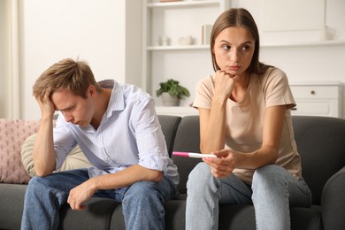 Photo of Worried couple with pregnancy test on sofa at home