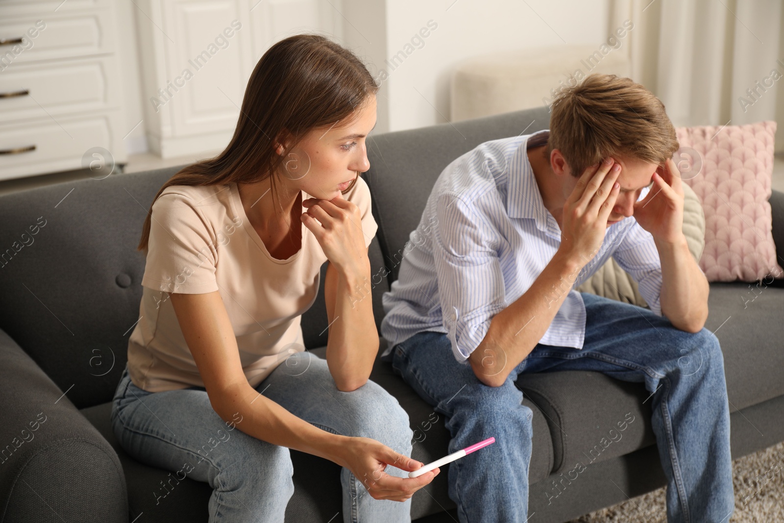 Photo of Worried couple with pregnancy test on sofa at home