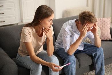 Photo of Worried couple with pregnancy test on sofa at home