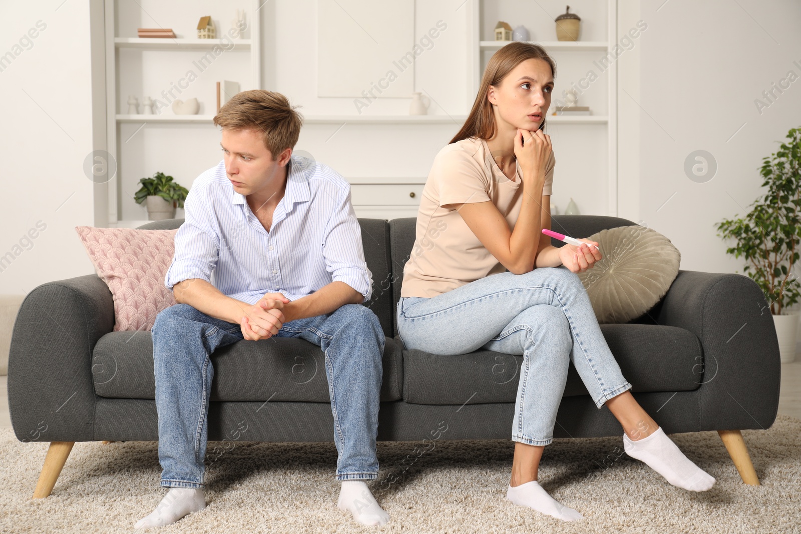 Photo of Worried couple with pregnancy test on sofa at home