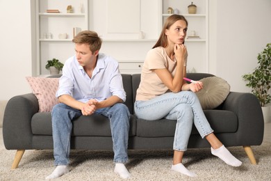 Photo of Worried couple with pregnancy test on sofa at home