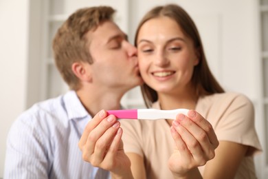 Photo of Happy couple with pregnancy test at home, selective focus