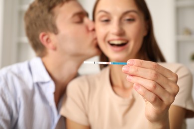 Photo of Happy couple with pregnancy test at home, selective focus