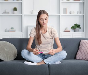 Photo of Worried young woman with pregnancy test on sofa at home