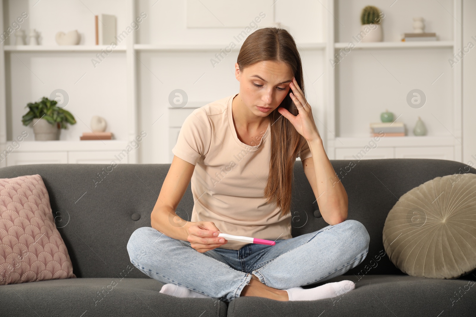 Worried young woman with pregnancy test on sofa at home Photo of Worried young woman with pregnancy test on sofa at home