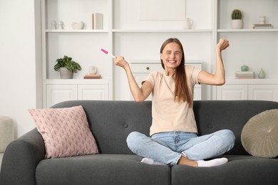 Photo of Happy young woman with pregnancy test on sofa at home