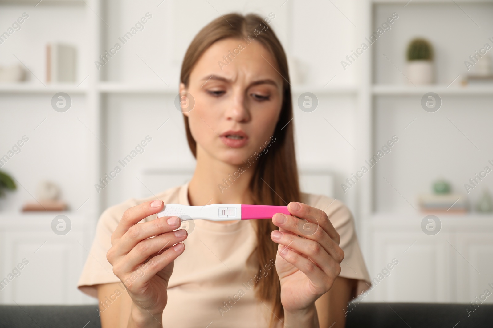 Worried young woman with pregnancy test indoors, selective focus Photo of Worried young woman with pregnancy test indoors, selective focus