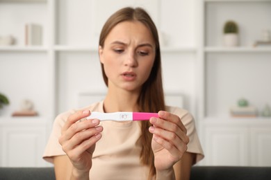 Photo of Worried young woman with pregnancy test indoors, selective focus