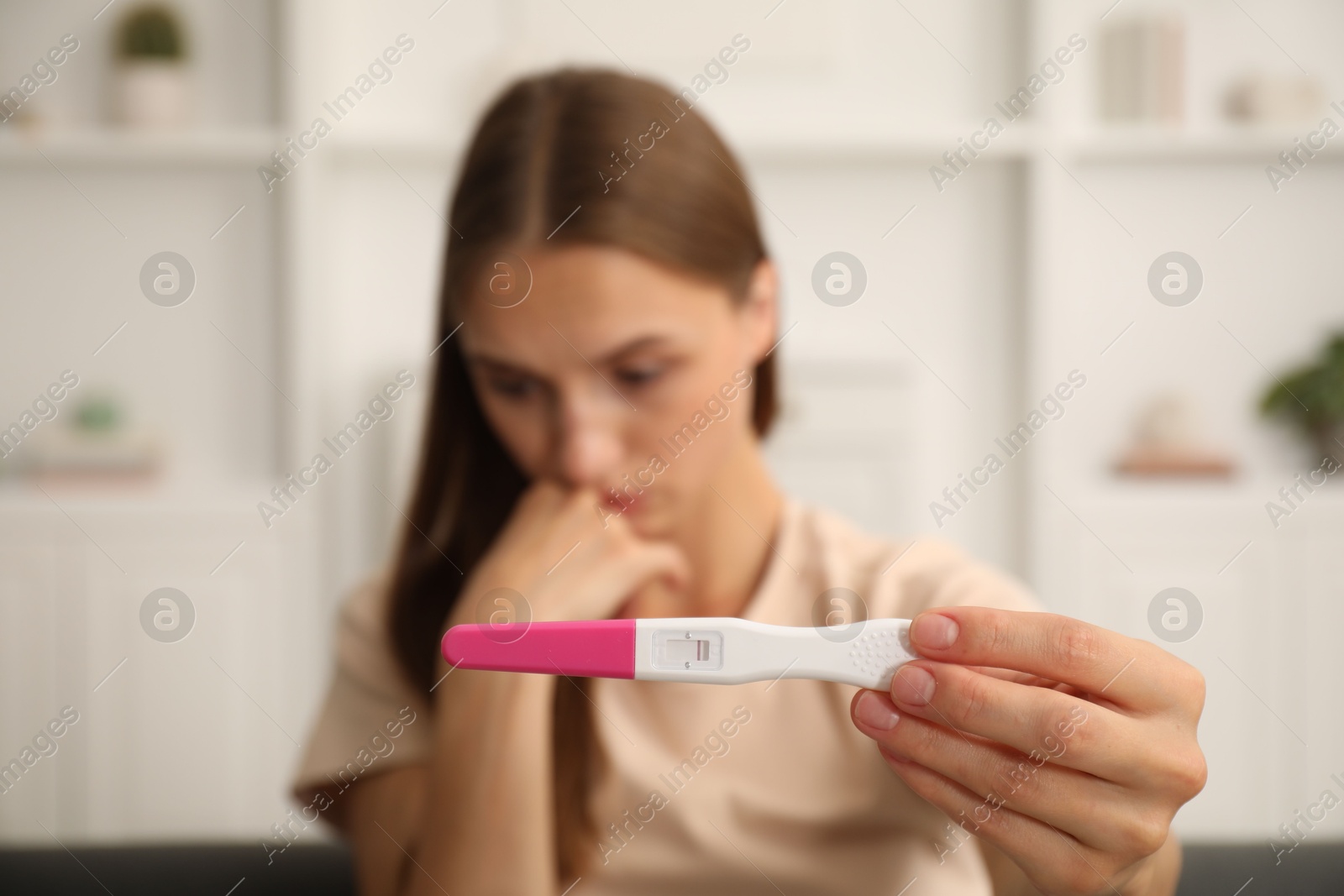 Worried young woman with pregnancy test indoors, selective focus Photo of Worried young woman with pregnancy test indoors, selective focus