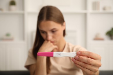 Photo of Worried young woman with pregnancy test indoors, selective focus
