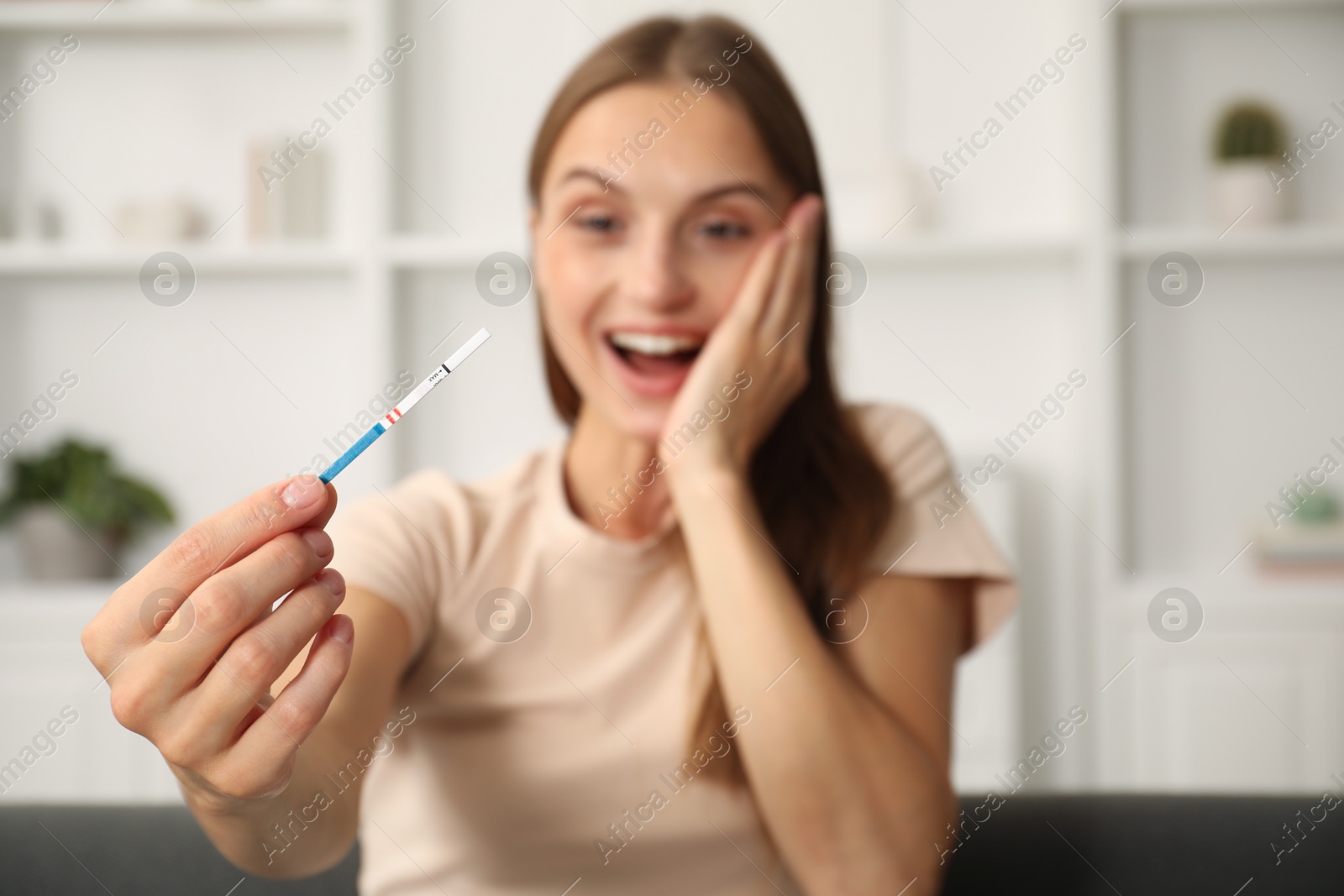 Happy young woman with pregnancy test indoors, selective focus Photo of Happy young woman with pregnancy test indoors, selective focus