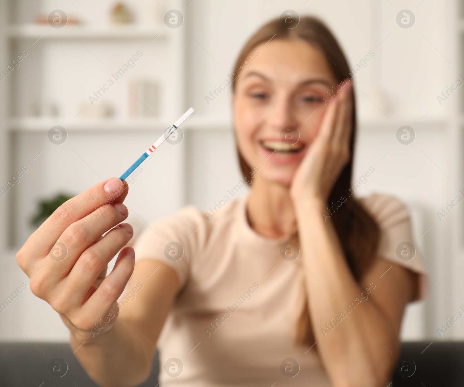 Happy young woman with pregnancy test indoors, selective focus Photo of Happy young woman with pregnancy test indoors, selective focus