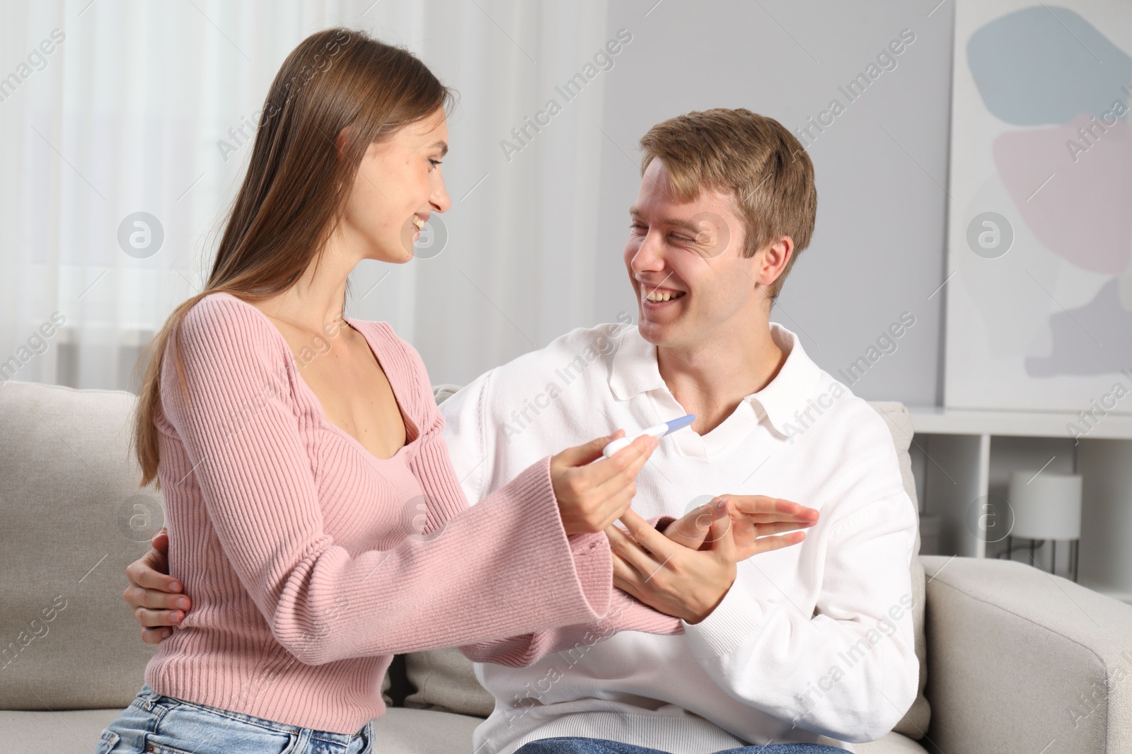 Happy couple with pregnancy test on sofa at home Photo of Happy couple with pregnancy test on sofa at home