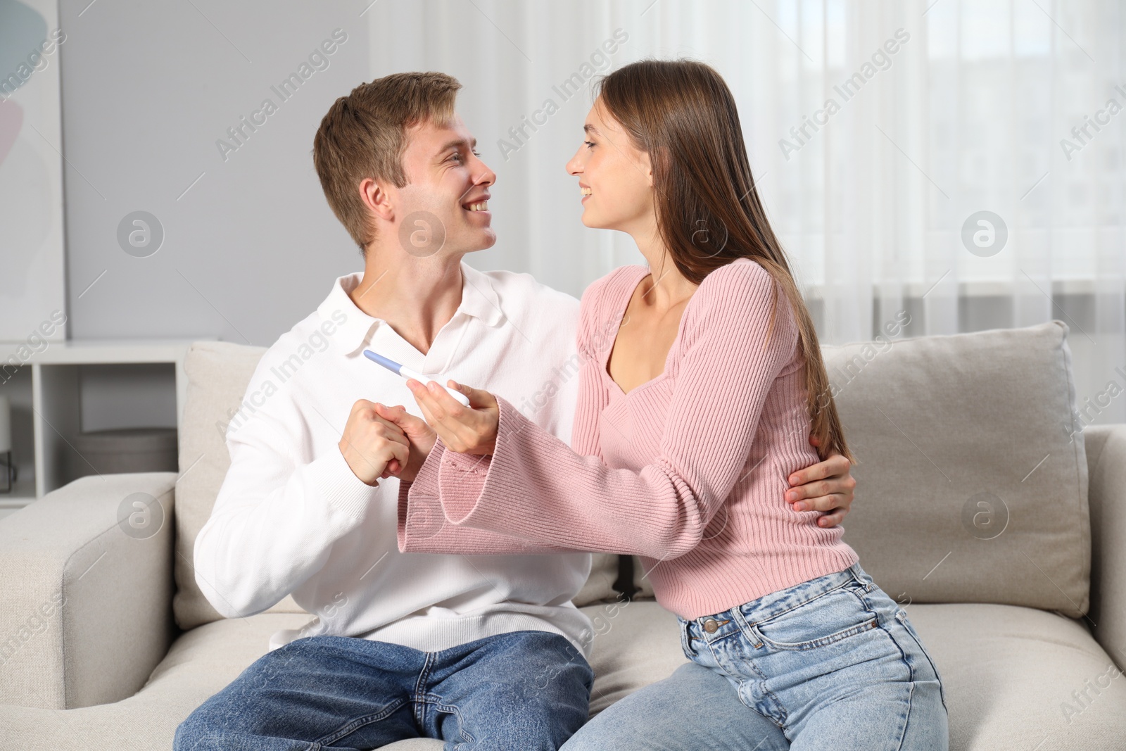 Photo of Happy couple with pregnancy test on sofa at home