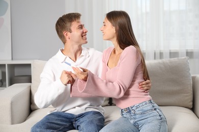Photo of Happy couple with pregnancy test on sofa at home