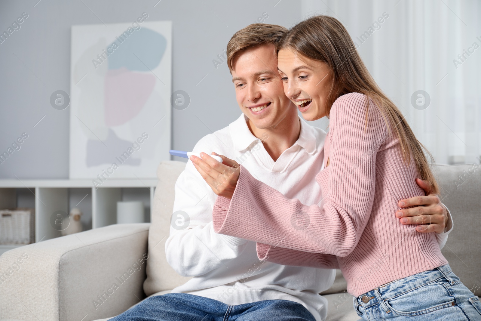 Happy couple with pregnancy test on sofa at home Photo of Happy couple with pregnancy test on sofa at home