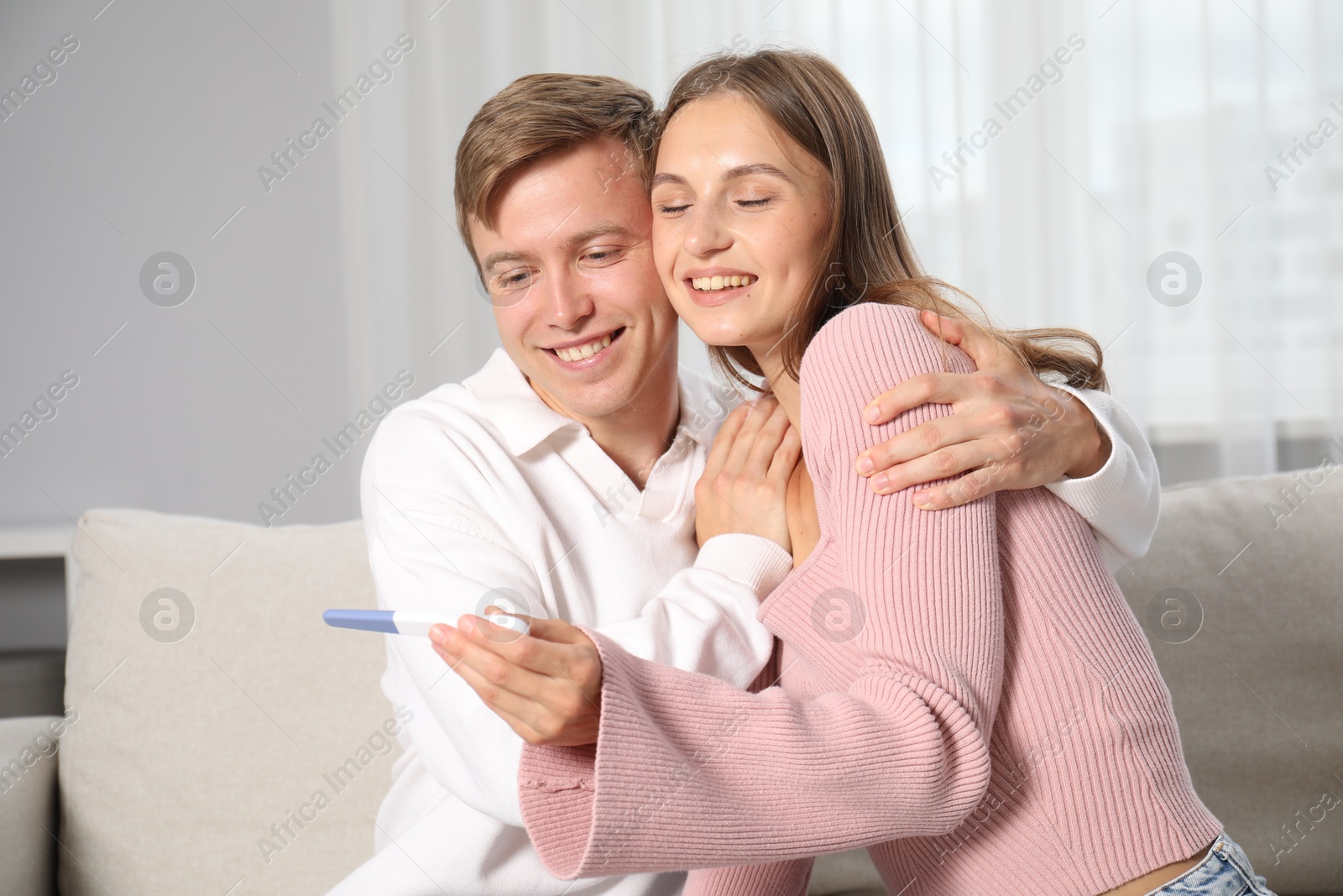 Happy couple with pregnancy test on sofa at home Photo of Happy couple with pregnancy test on sofa at home