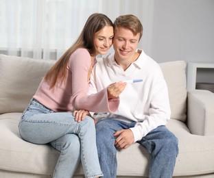 Photo of Happy couple with pregnancy test on sofa at home