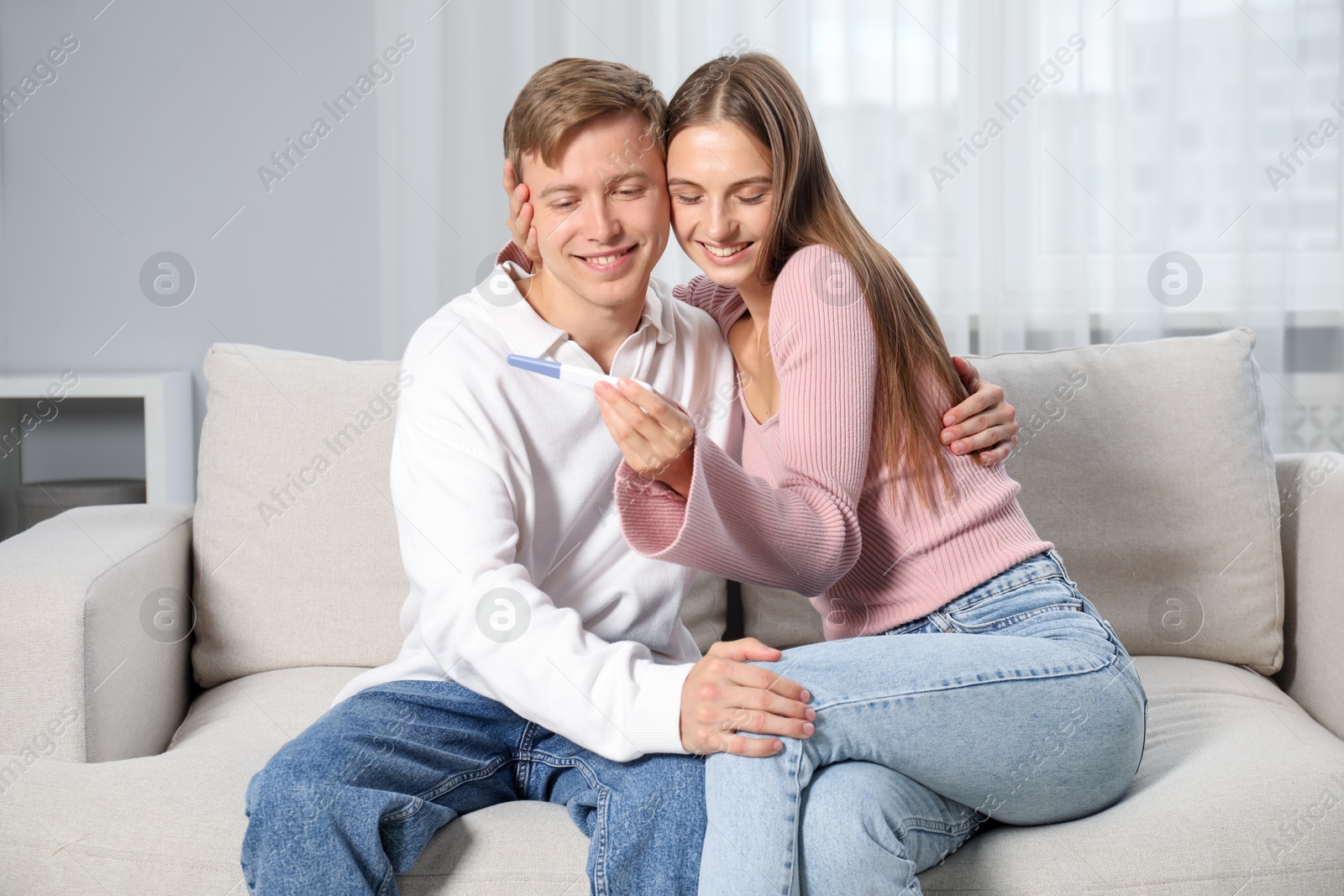 Happy couple with pregnancy test on sofa at home Photo of Happy couple with pregnancy test on sofa at home