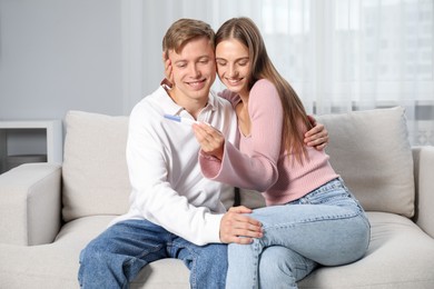 Photo of Happy couple with pregnancy test on sofa at home