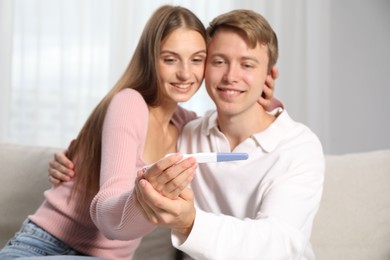 Photo of Happy couple with pregnancy test on sofa at home