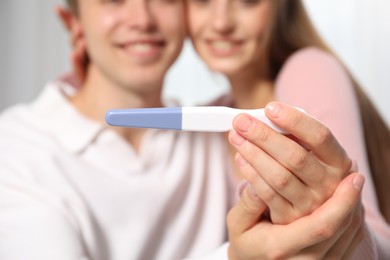 Photo of Happy couple with pregnancy test at home, selective focus
