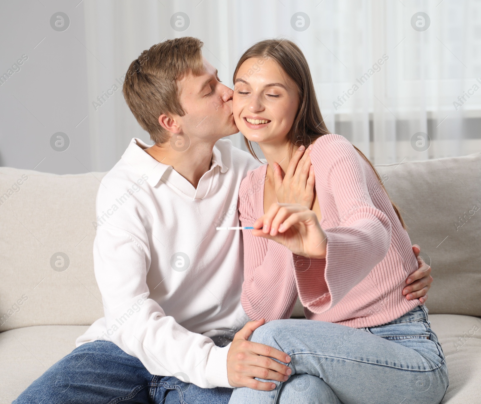 Happy couple with pregnancy test on sofa at home Photo of Happy couple with pregnancy test on sofa at home