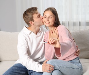 Photo of Happy couple with pregnancy test on sofa at home