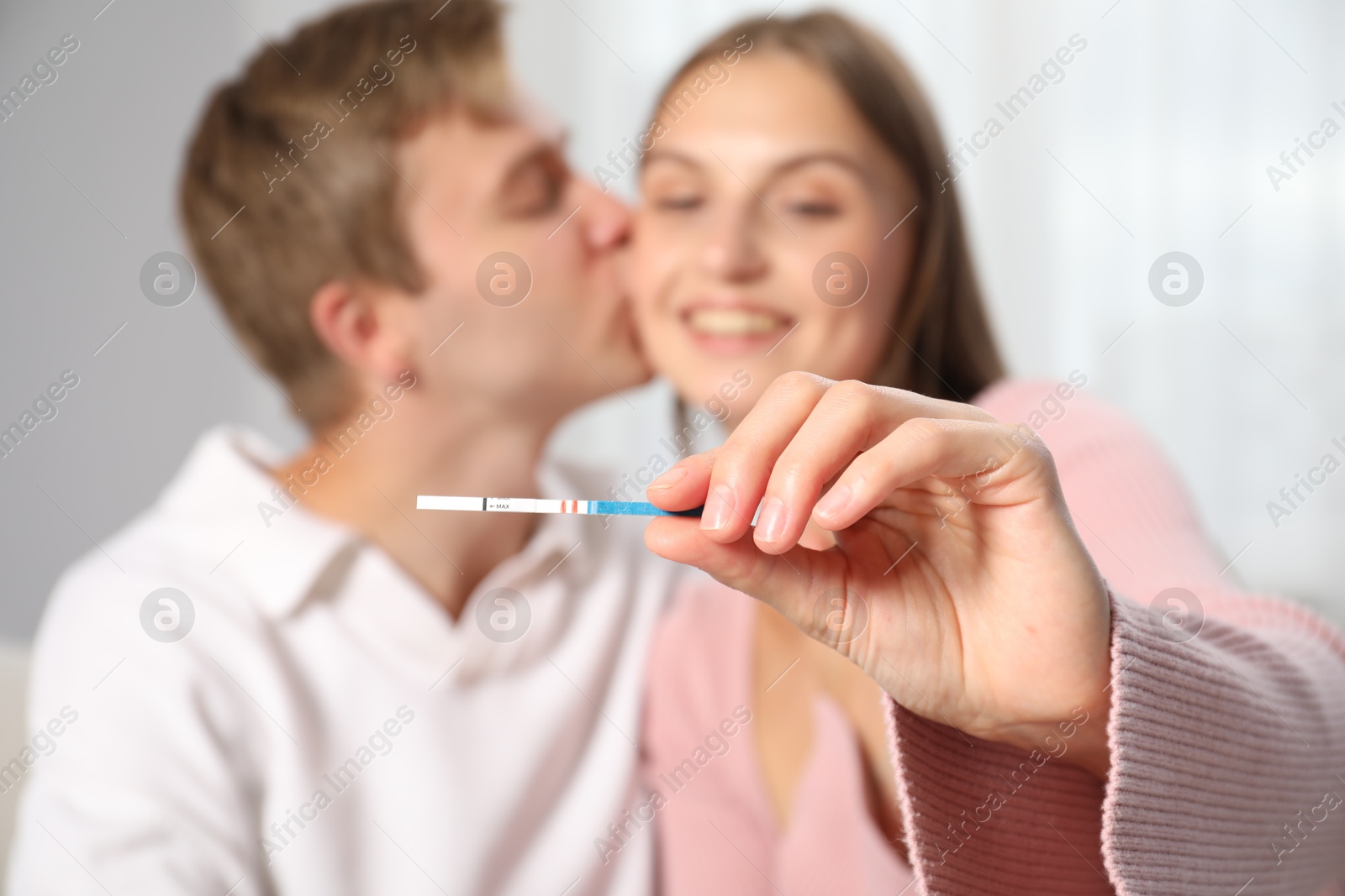 Photo of Happy couple with positive pregnancy test at home, selective focus
