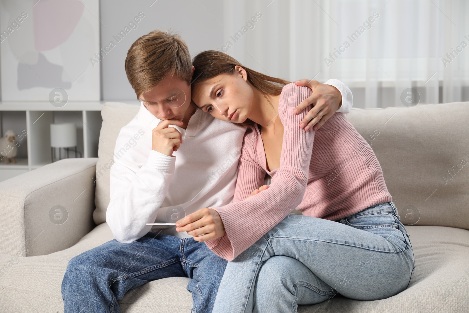 Worried couple with pregnancy test on sofa at home Photo of Worried couple with pregnancy test on sofa at home