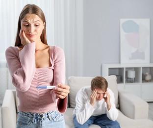 Photo of Worried woman with pregnancy test and her husband at home, selective focus