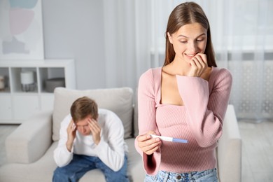 Photo of Emotional woman with pregnancy test and her husband at home, selective focus
