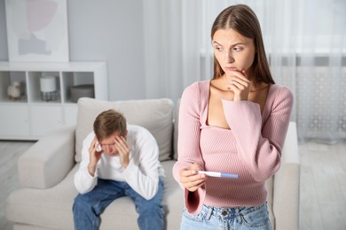 Photo of Worried woman with pregnancy test and her husband at home, selective focus